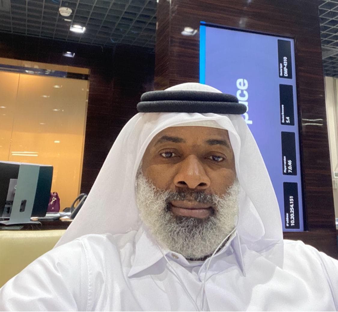 A man with a grey beard wearing traditional white Arab clothing in an office.